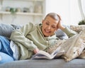 Cheerful happy woman reading book and smiling while relaxing on sofa at home Royalty Free Stock Photo