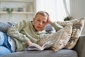Cheerful happy woman reading book and smiling while relaxing on sofa at home Royalty Free Stock Photo