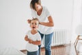 Funny moment of real life when young mother doing to her daughter toddler girl pony tail in the bright room Royalty Free Stock Photo
