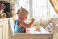 Funny naughty baby eating alone in the high chair