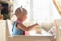 Funny naughty baby eating alone in the high chair