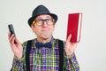 Funny nerd with glasses with book and mobile phone. Playful man in checkered shirt and black hat. Excited man having an idea. Male