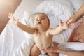 Funny nice little baby girl stretching hands to camera sitting on bed with mom at home.