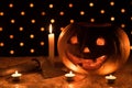 A funny orange pumpkin like a head with carved eyes and a smile with candles and an ax on a black background with a garland for Royalty Free Stock Photo