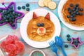 Funny pancakes for children. Cat shaped pancake on white plate, blue wooden background, top view. Creative idea for kids Royalty Free Stock Photo