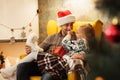 Funny photo of little girl touching with finger nose of her father, while sitting on his knees in living room with Christmas decor