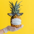 Funny pineapple face in protective medical mask. Doctor hand in rubber glove holds summer tropical fruit pineapple in Royalty Free Stock Photo