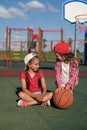 Funny playful girls with basketball are sitting on the sports court relaxing after the game