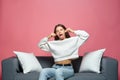 Funny playful young girl making silly monkey face bulging ears showing tongue, teasing, fooling, sitting on sofa Royalty Free Stock Photo