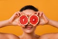 Funny playful young woman in checkered shirt holding halves of citrus fruits against her eyes and making duck face over yellow Royalty Free Stock Photo