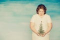 Funny plump red-haired girl in a white dress looks downcastly at the pathetic Christmas tree in her hands Royalty Free Stock Photo