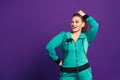 Funny plus size model in tracksuit shows her tongue, cheerful fat woman on purple background