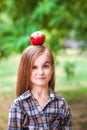 Funny portrait of a beautiful baby girl with a red apple on her head. A girl in a plaid shirt on a farm harvesting apples smiles a