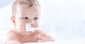 Funny portrait of cute toddler boy lying on bed and trying to eat a paper napkin. Newborn child in bedroom. Baby lies on his tummy Royalty Free Stock Photo