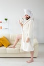 Funny portrait of handsome beautiful guy in towel and bathrobe holding tube of body cream lotion in hand. Spa, body and