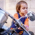 Funny portrait of little biker child girl looking in the rearview mirror and having fun on fashioned motorcycle. Humorous photo Royalty Free Stock Photo