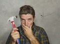 Funny portrait of man holding hammer after driving a nail for hanging a frame but making a mess cracking the wall as a disaster