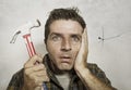 Funny portrait of man holding hammer after driving a nail for hanging a frame but making a mess cracking the wall as a disaster