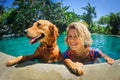 Young woman relaxing with golden retriever in tropical swimming pool