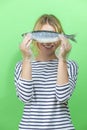 Funny Portrait of Winsome Beautiful Caucasian Young Girl Holding Freshly Frozen Mackerel in Front of Face on Green Background