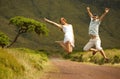 Jumping happy young couple in honneymoon. Just married jumping on countriside road. Background of lush green hills