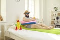 Funny bearded man with travel accessories lying in bed imagining resort vacation