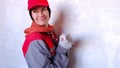 A funny and positive woman in a cap and work uniform poses with a spatula against the background of a wall for repairing and finis