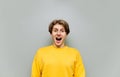 Funny positive young man stands in yellow clothes on a gray background and looks into the camera with his mouth open and happy Royalty Free Stock Photo