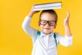 Funny Preschool Child Boy in Glasses with Book on Head and Bag on Yellow Background Copy Space. Happy Smiling Kid Go Royalty Free Stock Photo