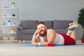 Funny red fat man doing exercises on the floor smiling while lying on the floor at home. Royalty Free Stock Photo