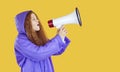 Funny red-haired beautiful young woman, dressed in raincoat, sings into megaphone. Royalty Free Stock Photo