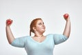 Funny red haired, chubby woman is smiling and holding dumbbells