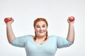 Funny red haired, chubby woman is smiling and holding dumbbells