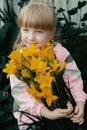 Funny red-haired girl with a bouquet of yellow lilies laughs. Portrait of a cheerful child Royalty Free Stock Photo