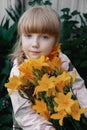 Funny red-haired girl with a bouquet of yellow lilies laughs. Portrait of a cheerful child Royalty Free Stock Photo