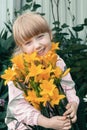 Funny red-haired girl with a bouquet of yellow lilies laughs. Portrait of a cheerful child Royalty Free Stock Photo