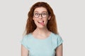 Funny red-haired girl in glasses play childish showing tongue