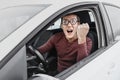 Ridiculous nerd driver in eyeglasses shouting to the camera and showing his fist inside a car. Concept of a newbie