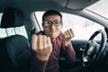 Ridiculous nerd driver in eyeglasses shouting to the camera and showing his fist inside a car. Concept of a newbie