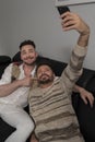 Funny romantic male gay couple using smartphone for video call. Family time in the living room