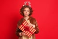 Funny sad unsatisfied woman in a Christmas reindeer costume with unsuccessful gift on colorful red background