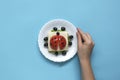 Funny sandwich for children in form of ladybug made of fresh tomato, salad, cheese, sausage, bacon and bread on blue background. Royalty Free Stock Photo