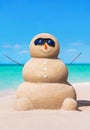 Funny sandy snowman in sunglasses at tropical sunny ocean beach.