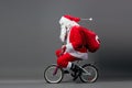 Funny Santa Claus in sunglasses and headphones with the bag with Christmas gifts on his back rides a bicycle on the