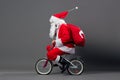 Funny Santa Claus in sunglasses and headphones with the bag with Christmas gifts on his back rides a bicycle on the