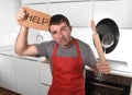 Funny scared man holding pan wearing apron at kitchen asking for help Royalty Free Stock Photo