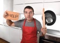 Funny scared man holding pan wearing apron at kitchen asking for help