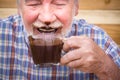 Funny scene with nice senior old man portrait drinking hot chocolate and having face dirty of it - mature people have fun ald