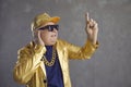Funny senior DJ in golden jacket, baseball cap and chain necklace mixing music at disco party