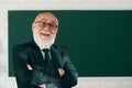 Funny Senior professor. Portrait of happy senior teacher with arms crossed standing against chalkboard. Royalty Free Stock Photo
